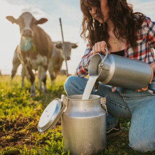 Young woman pouring raw milk into container while crouching in field